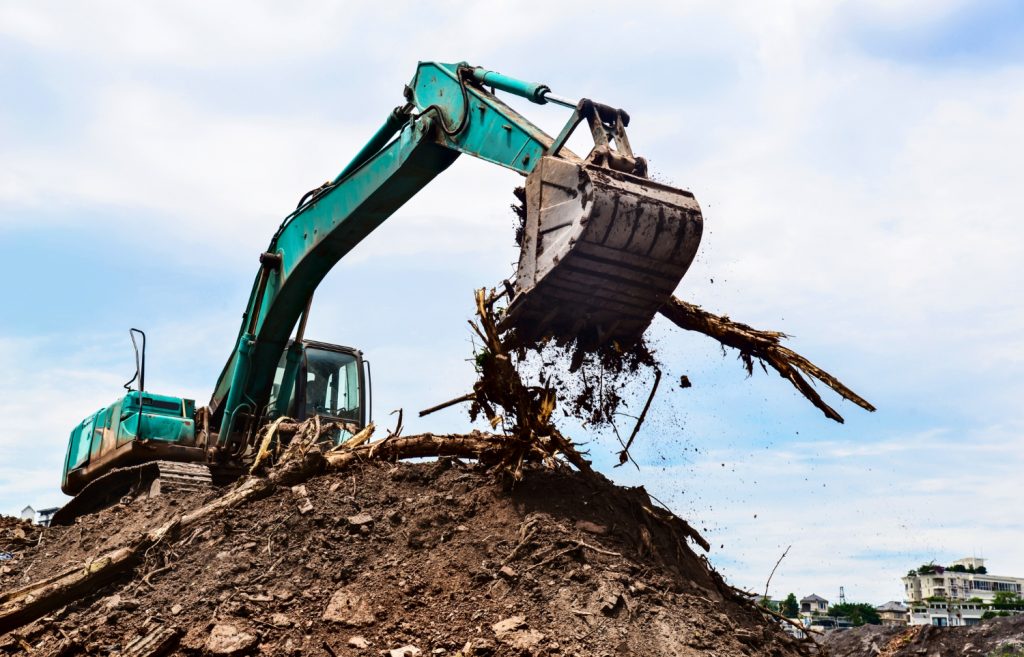 Excavator moving dirt and roots on a construction site